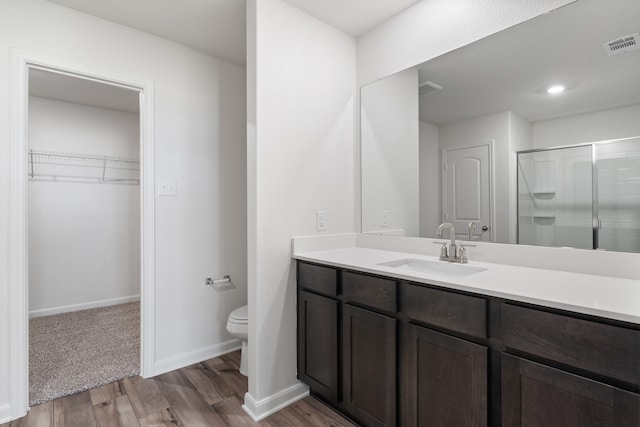 bathroom featuring toilet, a shower stall, wood finished floors, vanity, and a spacious closet