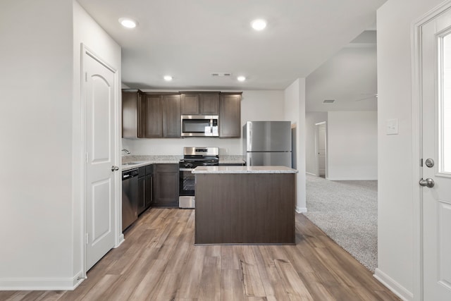 kitchen with stainless steel appliances, a kitchen island, dark brown cabinets, light wood finished floors, and recessed lighting