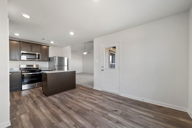 kitchen featuring stainless steel appliances, dark wood finished floors, dark brown cabinets, light countertops, and a center island