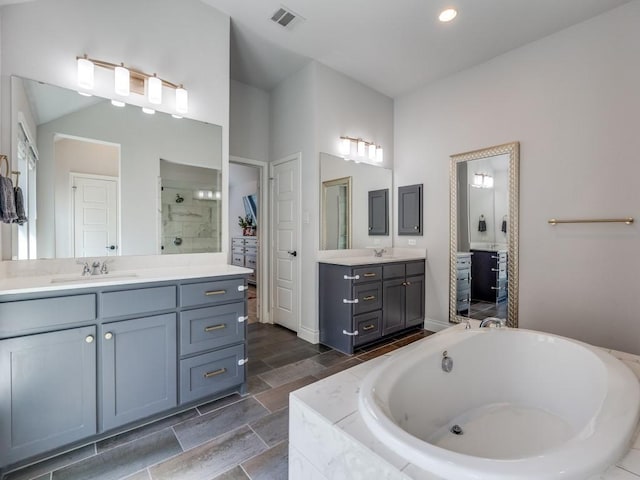 full bathroom featuring two vanities, tiled shower, a bath, visible vents, and a sink