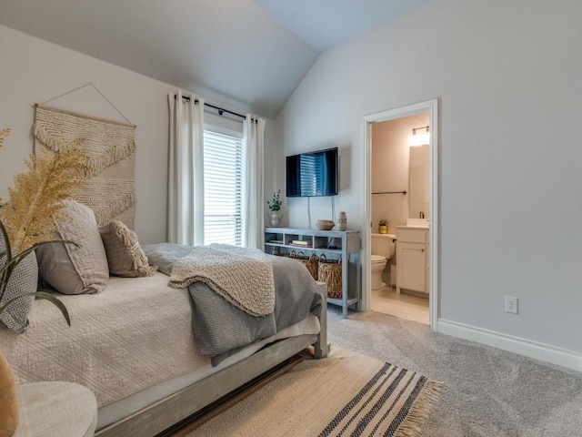 bedroom featuring baseboards, ensuite bathroom, light colored carpet, and vaulted ceiling