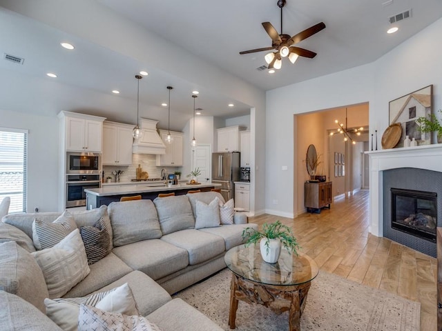 living area with visible vents, baseboards, light wood finished floors, and ceiling fan with notable chandelier