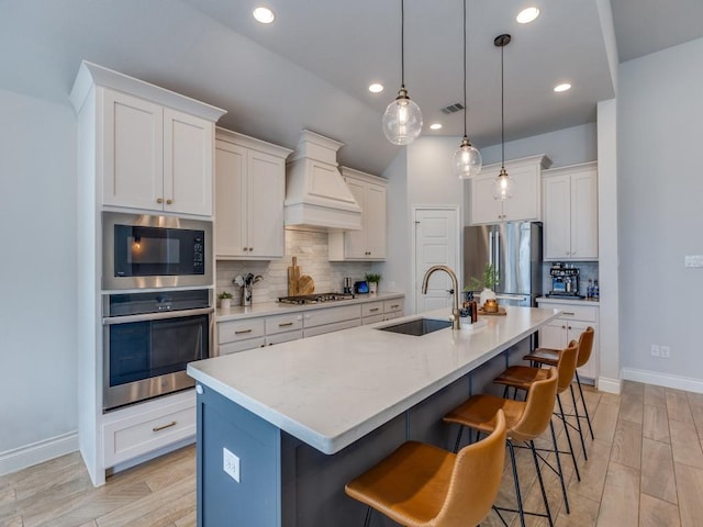 kitchen with a kitchen breakfast bar, visible vents, a sink, stainless steel appliances, and premium range hood