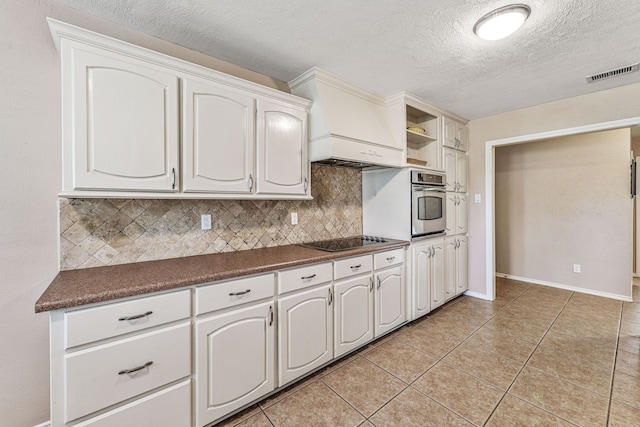 kitchen with stainless steel oven, backsplash, dark countertops, visible vents, and black electric cooktop
