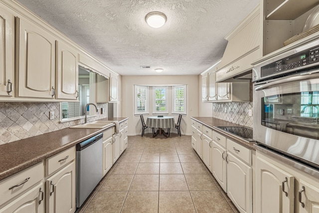 kitchen with cream cabinetry, appliances with stainless steel finishes, a sink, and dark countertops