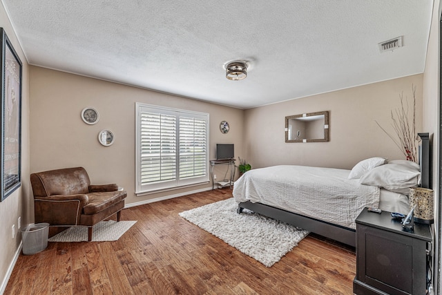 bedroom with visible vents, baseboards, a textured ceiling, and wood finished floors