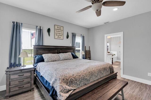 bedroom featuring visible vents, baseboards, ensuite bathroom, and wood finished floors