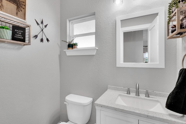half bathroom featuring toilet, vanity, and a textured wall