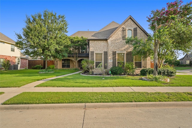 view of front of property featuring a front lawn, cooling unit, a shingled roof, and brick siding