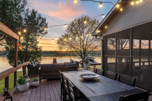 deck at dusk featuring a water view, outdoor dining space, and an outdoor hangout area