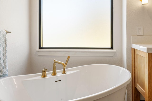 bathroom with a freestanding bath, a textured wall, and vanity