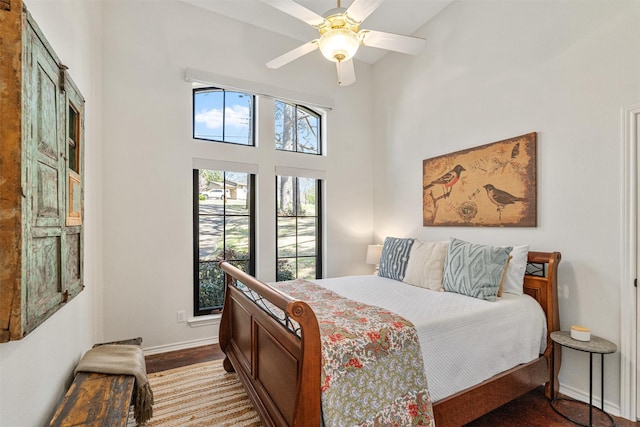 bedroom with baseboards, a ceiling fan, a high ceiling, and wood finished floors