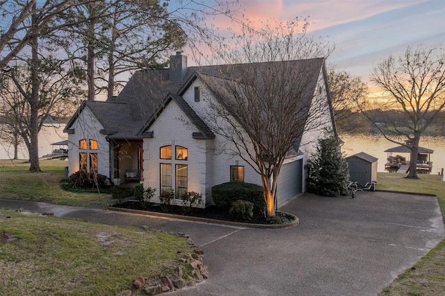 french country home featuring a chimney, driveway, a yard, and brick siding