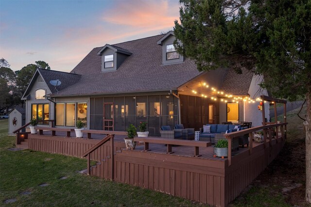 back of house at dusk featuring an outdoor living space, a sunroom, a lawn, roof with shingles, and a deck