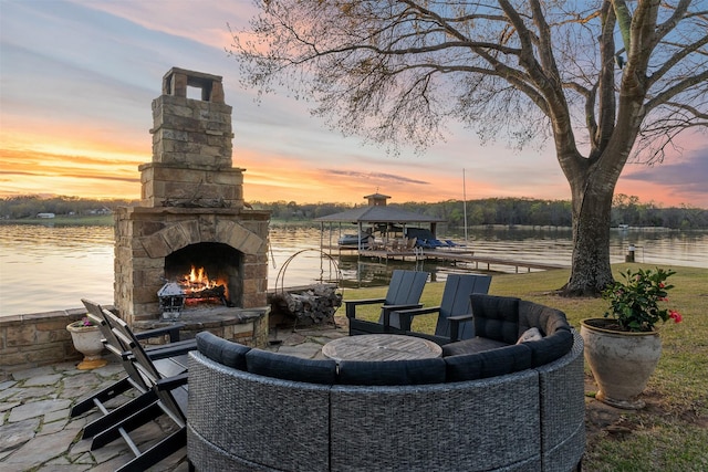 patio terrace at dusk with an outdoor stone fireplace and a water view