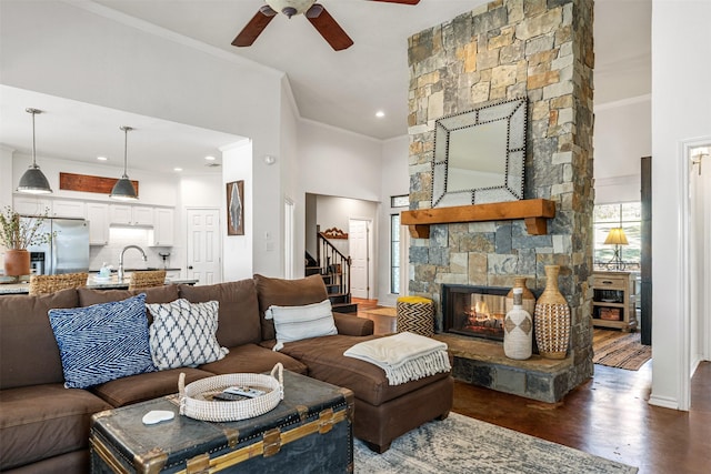 living room featuring a stone fireplace, ornamental molding, stairway, a ceiling fan, and dark wood-type flooring