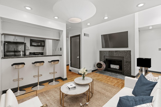 living room featuring light wood-type flooring, baseboards, a fireplace, recessed lighting, and visible vents