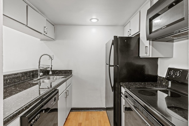 kitchen with dark stone counters, light wood-style flooring, white cabinetry, black appliances, and a sink