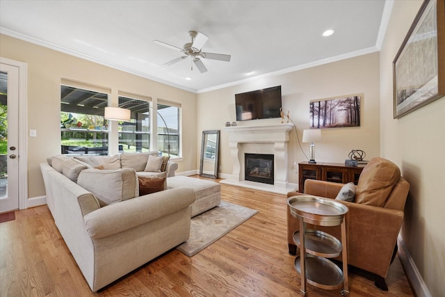 living area with a glass covered fireplace, wood finished floors, ornamental molding, and ceiling fan
