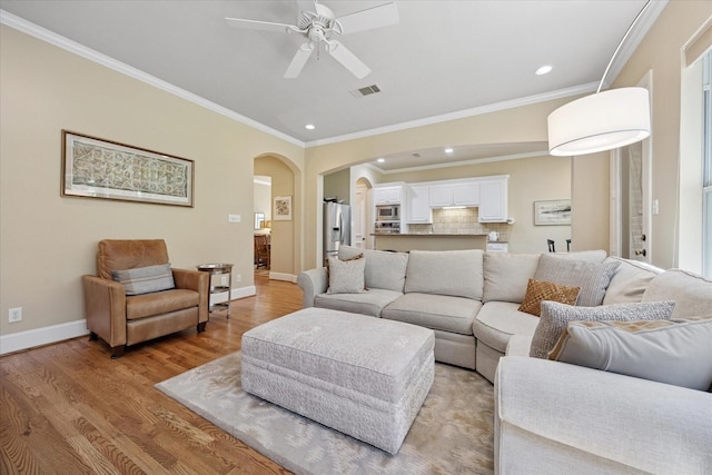 living room featuring crown molding, visible vents, ceiling fan, arched walkways, and light wood finished floors