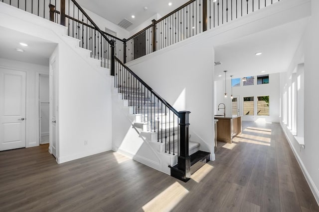 stairs with recessed lighting, a high ceiling, visible vents, baseboards, and wood finished floors