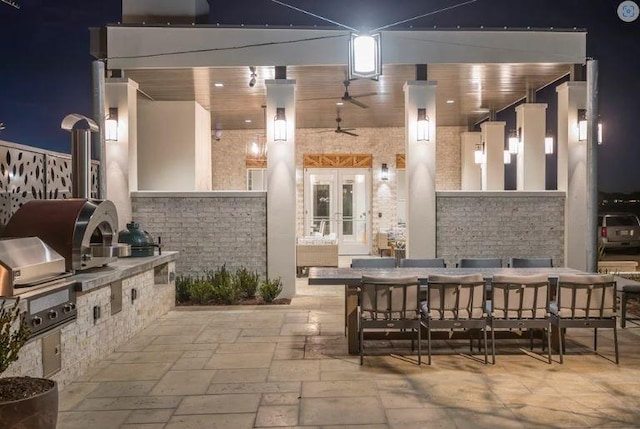 patio at night with outdoor dining space, exterior kitchen, french doors, and a grill
