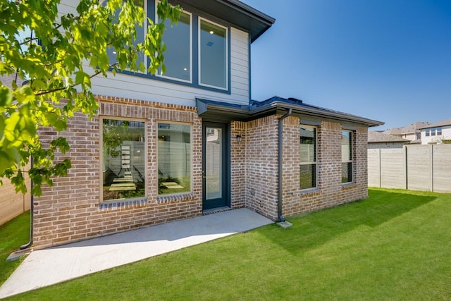rear view of property featuring brick siding, a yard, a patio area, and fence