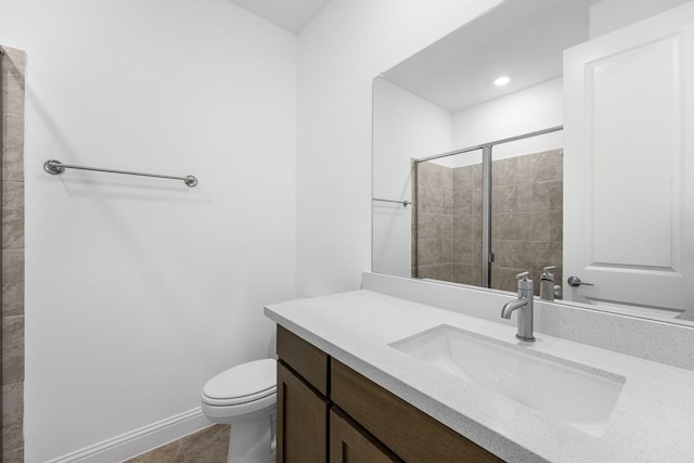 bathroom featuring toilet, a tile shower, vanity, and baseboards