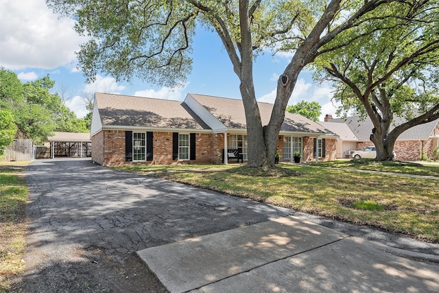 ranch-style home with a front yard, a carport, fence, brick siding, and driveway