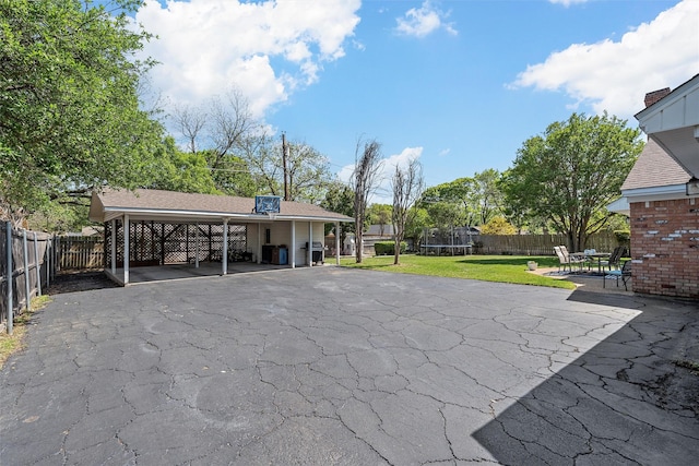 view of patio / terrace featuring a carport, a fenced backyard, a trampoline, and driveway