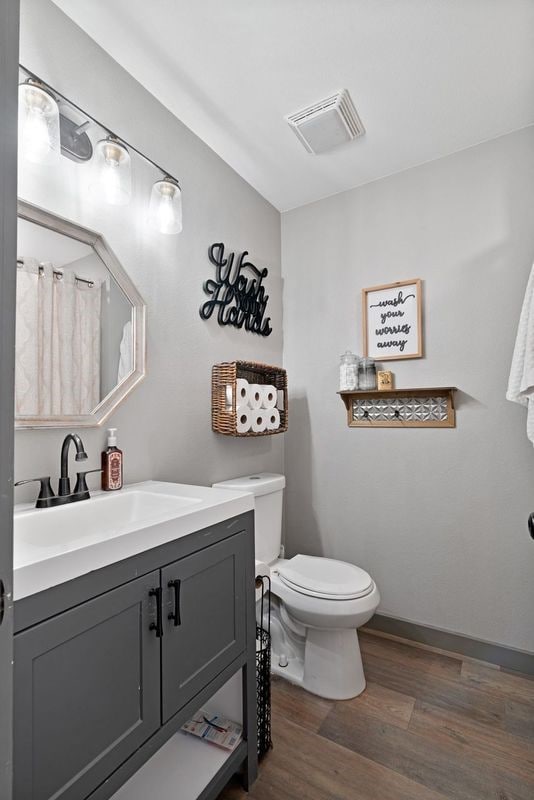 bathroom with vanity, baseboards, toilet, visible vents, and wood finished floors