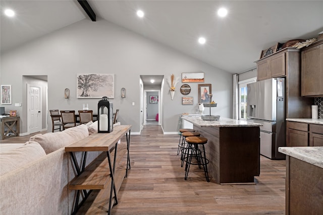 kitchen with a center island, stainless steel fridge, beam ceiling, high vaulted ceiling, and a breakfast bar area