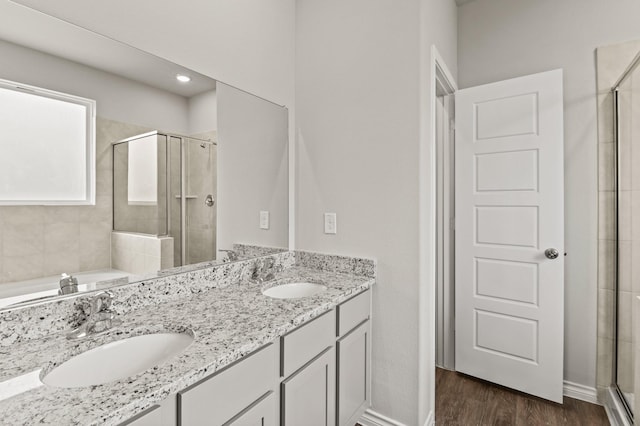 full bath with a shower stall, double vanity, a sink, and wood finished floors