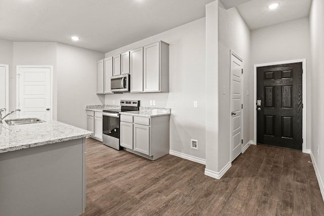 kitchen with light stone counters, dark wood-style flooring, a sink, stainless steel appliances, and baseboards