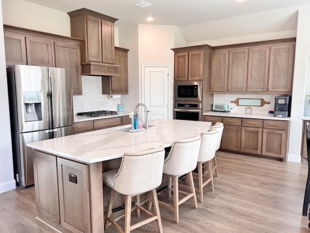 206 Lakewood Ln, Ponder, TX 76259 - kitchen featuring appliances with stainless steel finishes, a sink, backsplash, light wood-style floors, and a breakfast bar