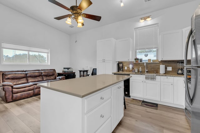 kitchen featuring a center island, a sink, ceiling fan, light wood finished floors, and decorative backsplash