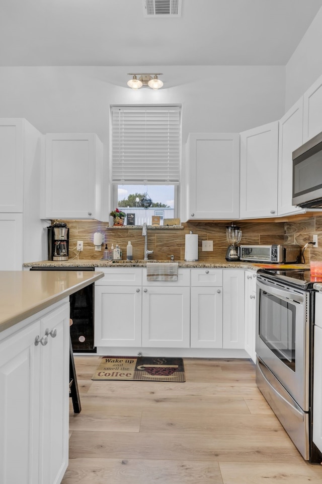 kitchen featuring a sink, appliances with stainless steel finishes, white cabinetry, decorative backsplash, and light stone counters