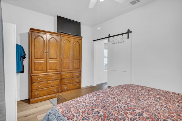 bedroom featuring ceiling fan, light wood-type flooring, visible vents, a barn door, and baseboards