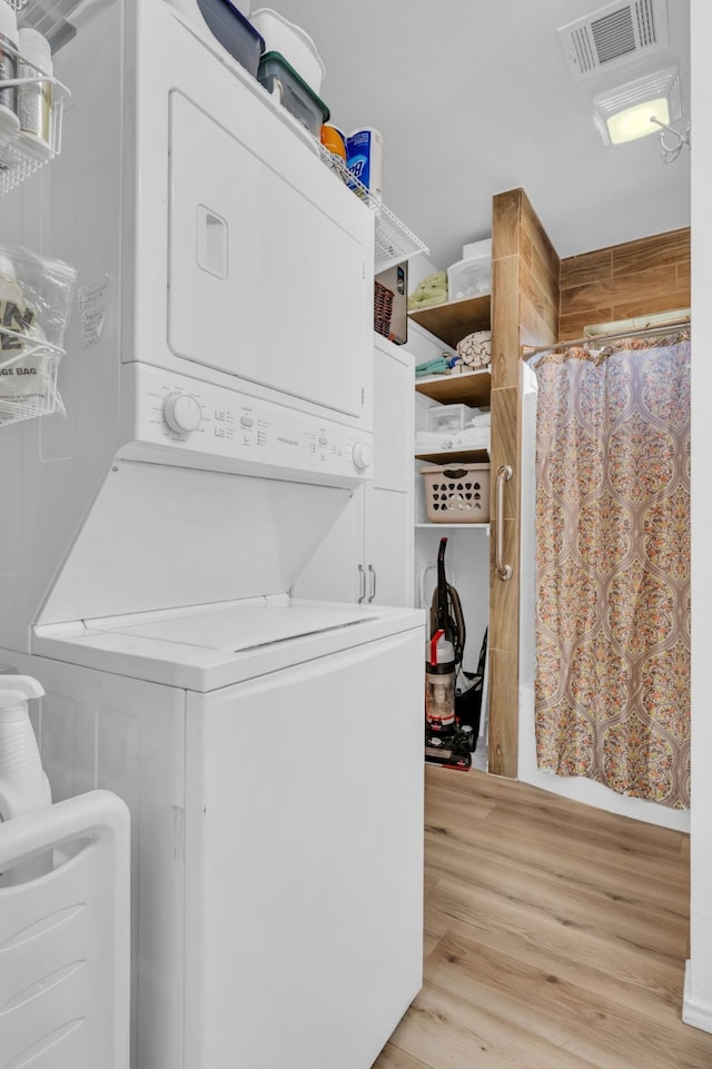 washroom with light wood finished floors, stacked washer / dryer, laundry area, and visible vents