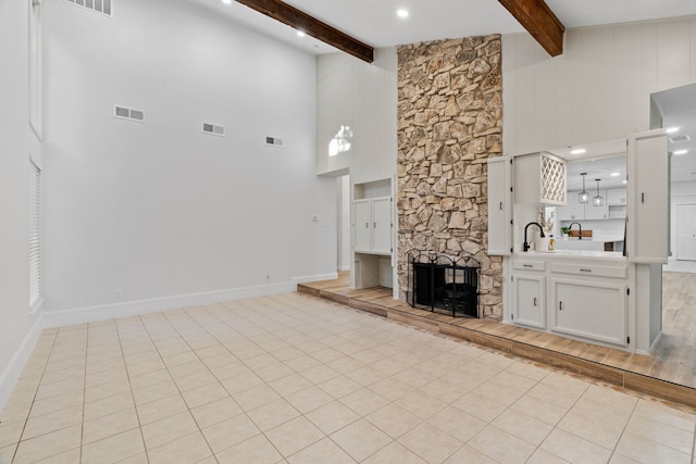 unfurnished living room featuring a sink, visible vents, beamed ceiling, and a high ceiling