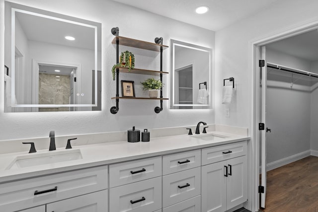 full bath with a walk in closet, wood finished floors, double vanity, and a sink