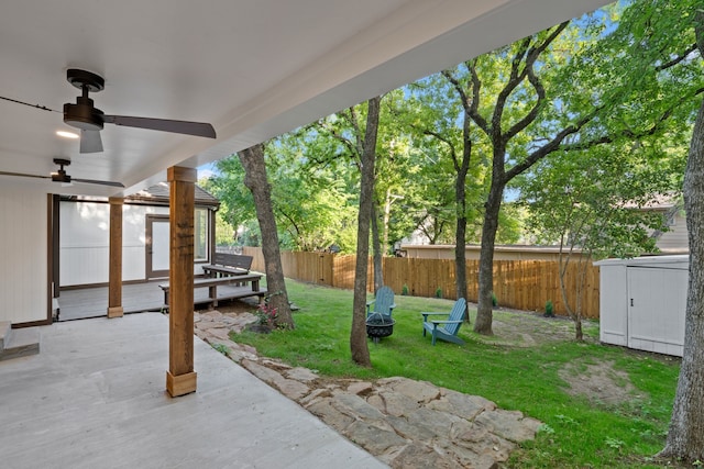 view of yard with a patio, an outdoor structure, a fenced backyard, a ceiling fan, and a storage unit