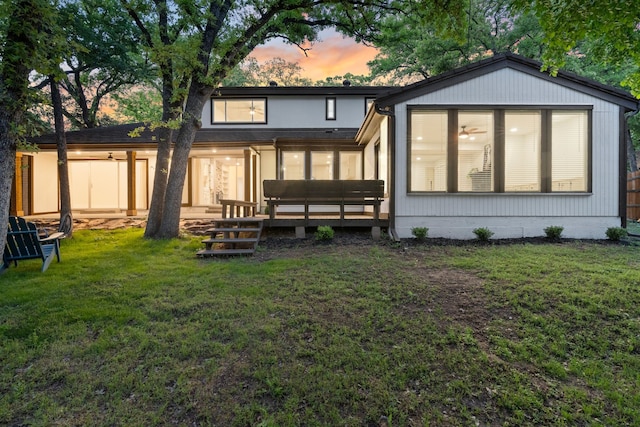 back of house at dusk featuring a wooden deck, a sunroom, and a lawn