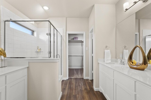 bathroom with vanity, baseboards, a stall shower, a spacious closet, and wood finished floors