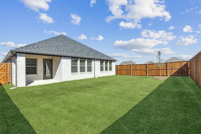 rear view of property featuring brick siding, roof with shingles, a fenced backyard, and a lawn