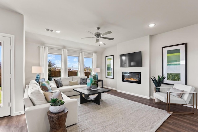 living area featuring a glass covered fireplace, visible vents, dark wood-style flooring, and a ceiling fan