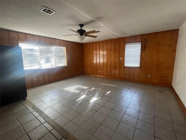 tiled spare room with visible vents, a wealth of natural light, a ceiling fan, and baseboards