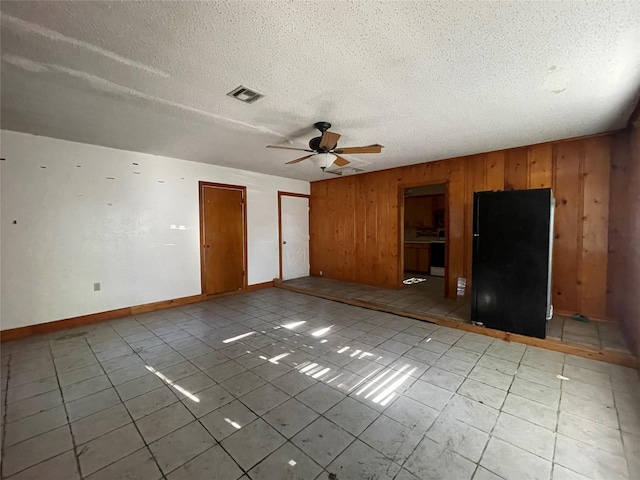 unfurnished bedroom with wooden walls, a textured ceiling, freestanding refrigerator, visible vents, and multiple closets
