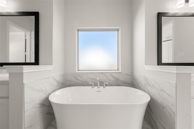 full bathroom with a freestanding tub, marble finish floor, wainscoting, and tile walls