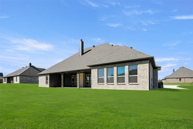 rear view of property featuring brick siding, a yard, a shingled roof, and a chimney